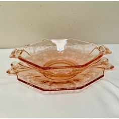 three pink glass dishes sitting on top of a white tablecloth covered table with a white wall in the background