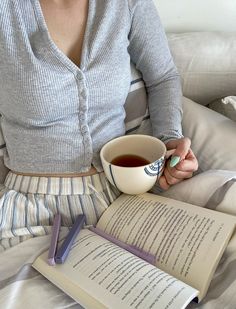 a woman sitting on a bed holding a cup of coffee and an open book