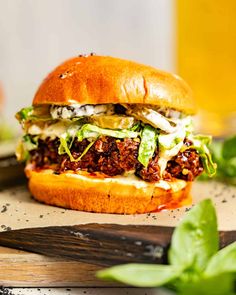 a sandwich with meat, lettuce and cheese on a cutting board next to a glass of beer