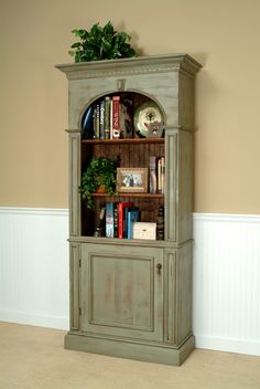 an old green bookcase with books and plants on top is in the corner of a room