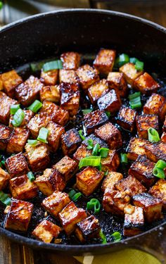 tofu in a skillet with green onions and seasoning on the side, ready to be eaten