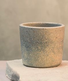 a white and grey cup sitting on top of a rock slab with a gray wall in the background