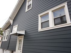 the side of a gray house with white trim on it's windows and shutters