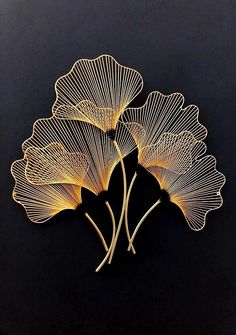 three golden metal leaf sculptures on a black surface, one is shaped like a fan