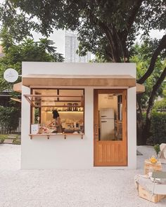 a small white building with a woman standing in the window and cooking food on an outdoor grill