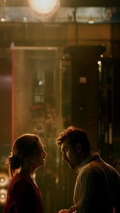 a man and woman standing next to each other in front of a building at night