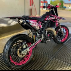 a pink and black motorcycle parked on top of a metal grate