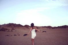 a woman in a white dress is walking through the desert with her arms spread out