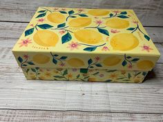 a yellow box with lemons painted on the side and flowers in the bottom, sitting on a wooden surface