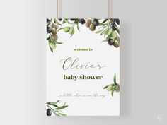 a welcome sign with olives hanging from the side on a white wall and green leaves