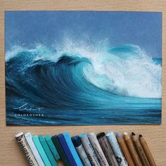 an image of a wave in the ocean on a wooden table with markers and pencils