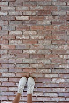 a person standing in front of a brick wall with their feet propped up on the ground