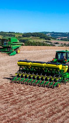 two green tractors are in the middle of a field