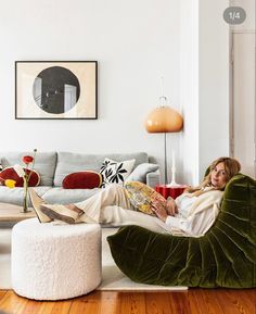 a woman laying on top of a green chair in a living room next to a white ottoman