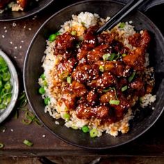 two bowls filled with rice and meat on top of a wooden table next to green beans