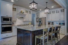 a kitchen with white cabinets and an island in the middle is lit by two pendant lights