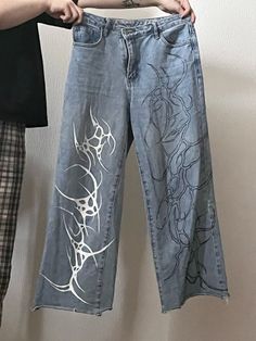 a person holding up a pair of jeans with designs on them