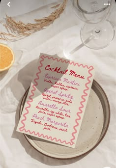 a menu on a plate next to an orange slice and wine glass with the name cocktail menu written on it