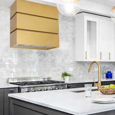 a kitchen with marble counter tops and gold hood over the stove, along with white cabinets