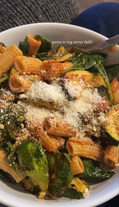 a white bowl filled with pasta and spinach covered in parmesan sprinkles