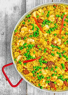 a paella with shrimp, peas and carrots in it on a wooden table