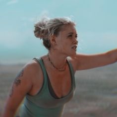 a woman holding a tennis racquet on top of a dry grass covered field