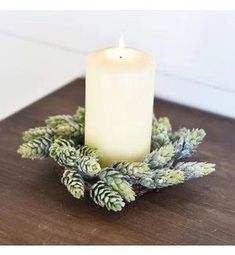 a lit candle sitting on top of a wooden table next to pine cones and greenery