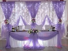 the table is covered with purple cloths and white flowers on it's side