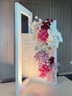 a white sign with flowers on it sitting in front of a wall that says welcome