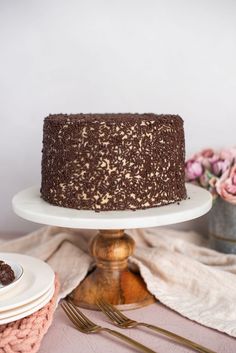 a chocolate cake sitting on top of a white plate next to pink flowers and silverware