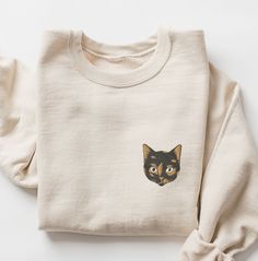 a white sweater with a black cat embroidered on the front and back, sitting on a white surface