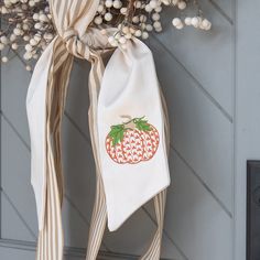 an orange pumpkin is hanging on the front door, with white berries and green leaves