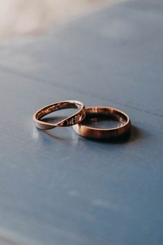 two gold wedding rings sitting on top of a blue table next to each other,