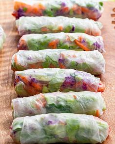 four rolls filled with vegetables sitting on top of a wooden cutting board