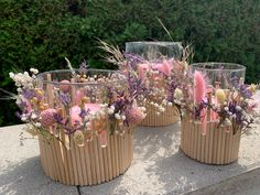 three vases filled with flowers on top of a cement wall next to trees and bushes