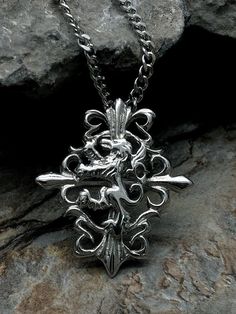 a silver necklace with an ornate design on the front and back of it, sitting on top of a rock