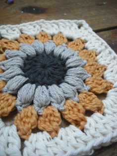 a crocheted square with an orange and gray flower on it sitting on a wooden surface