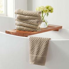 a stack of towels sitting on top of a bath tub next to a vase with flowers