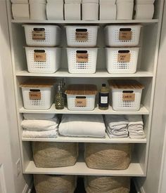 an organized pantry with baskets, towels and other items in white bins on shelves