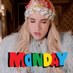 a woman with long blonde hair wearing a colorful hat and fur coat, standing in front of the words monday