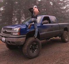 a woman sitting on the back of a blue truck with her arms in the air