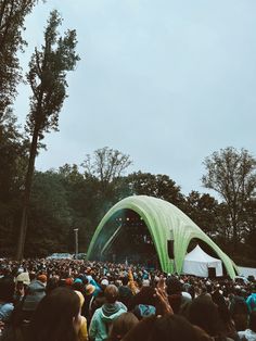 a large group of people standing in front of a green tent at a music festival