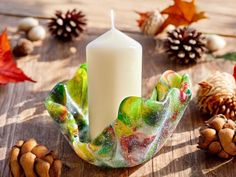 a white candle sitting on top of a wooden table next to pine cones and leaves