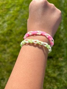 a person wearing a pink, white and green bracelet on their arm with grass in the background