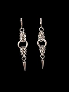 two silver earrings with spikes and chains hanging from it's sides on a black background