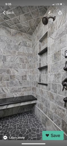 a walk in shower sitting next to a stone tiled wall and shelf with pictures on it