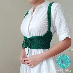 a woman wearing a white dress and green crochet suspenders with her hands in her pockets