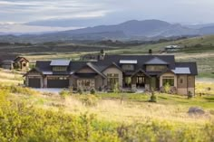 a large house in the middle of a grassy field with mountains in the back ground