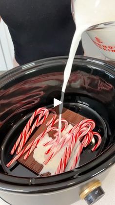 candy canes are being poured into an electric crockpot with chocolate and marshmallows