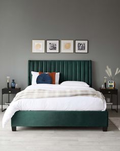 a bed with blue headboard and white sheets in a gray room next to two pictures on the wall